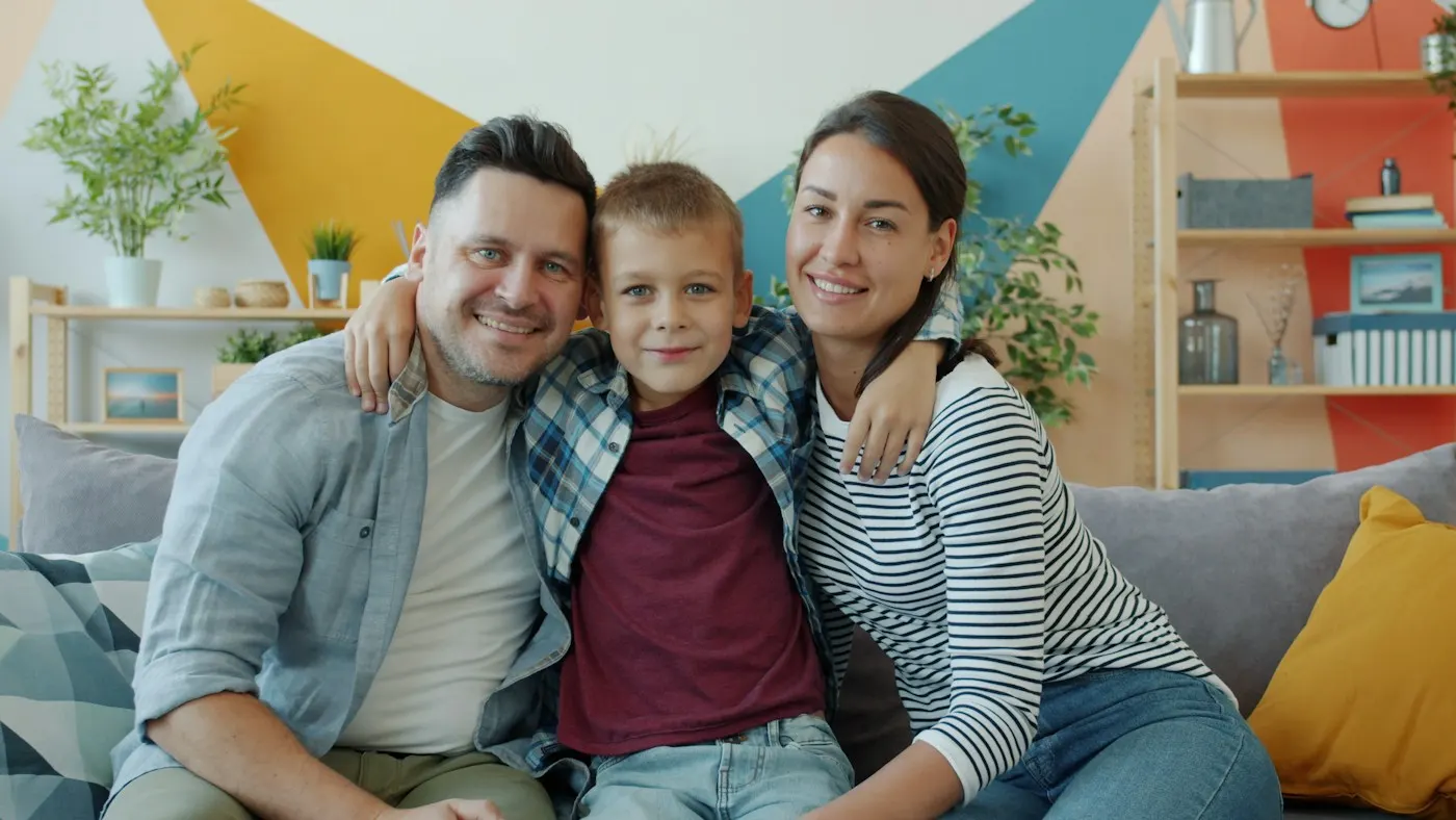 A mother, father and young son hugging on a sofa