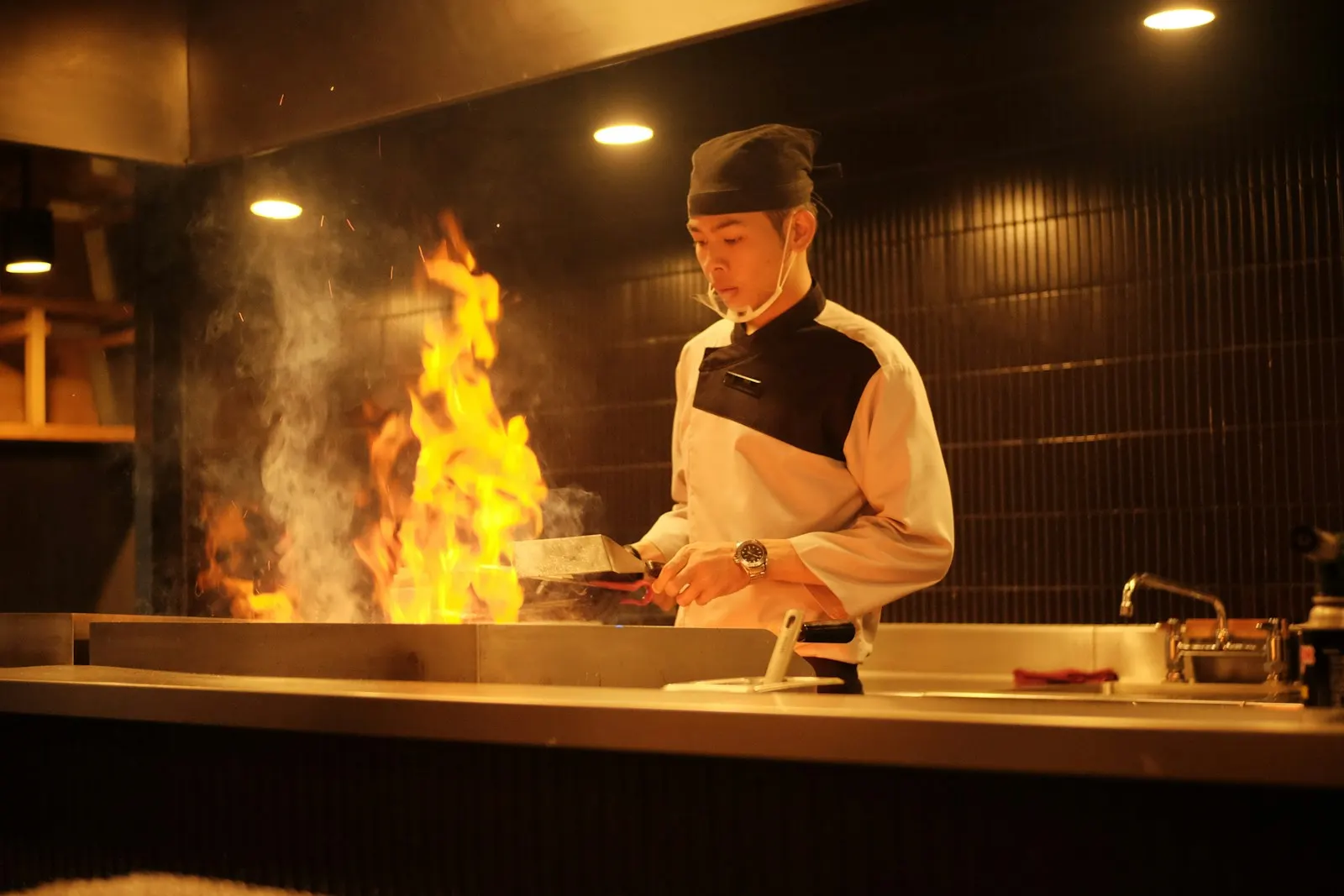 A chef working over tall flames on the open grill