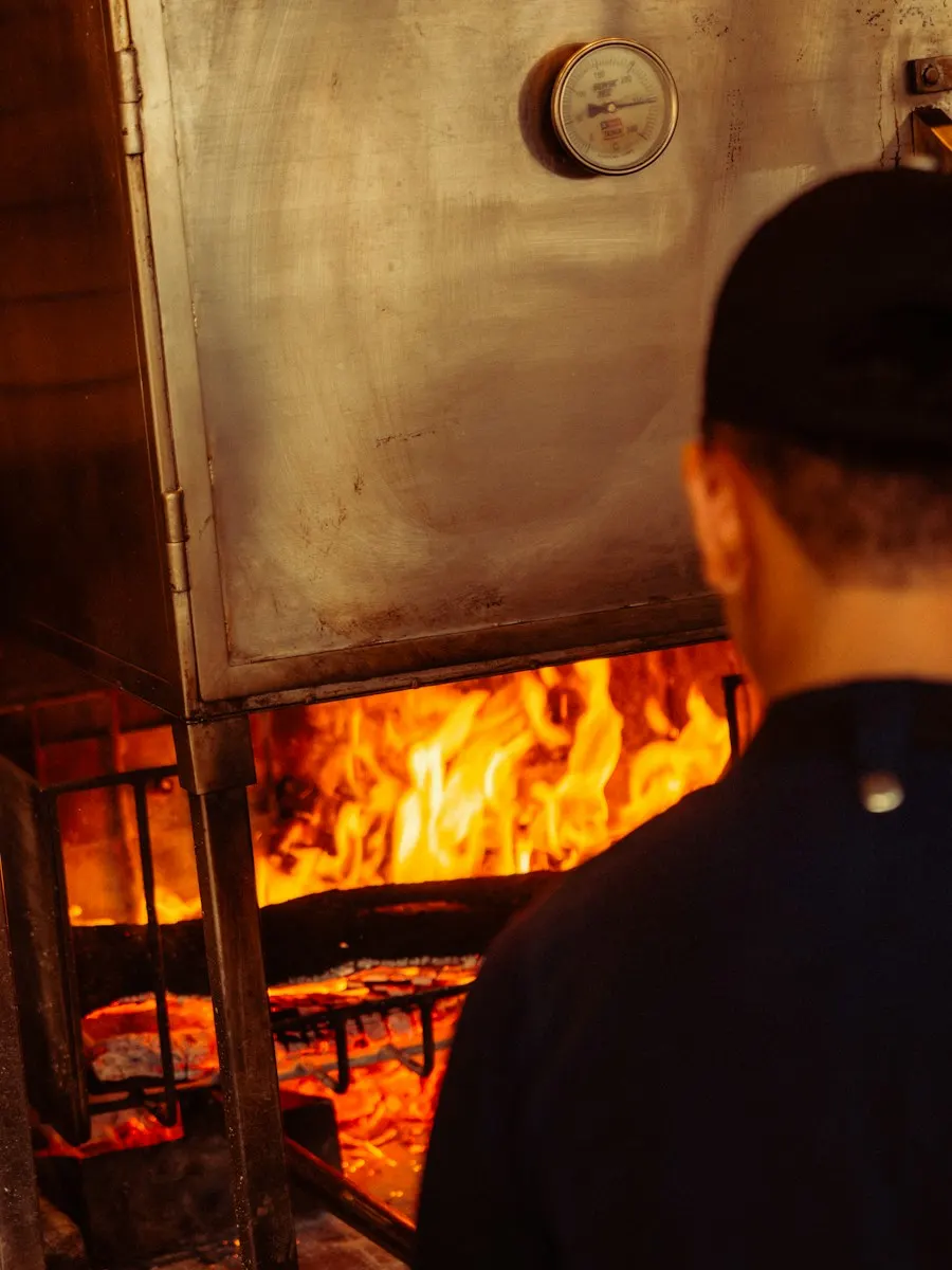 A cook tending the coals in the wood-fired grill