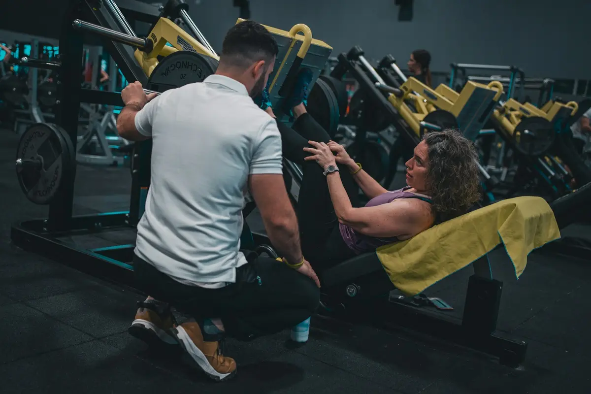 Coach kneeling beside a new member on a leg press, talking her through the movement