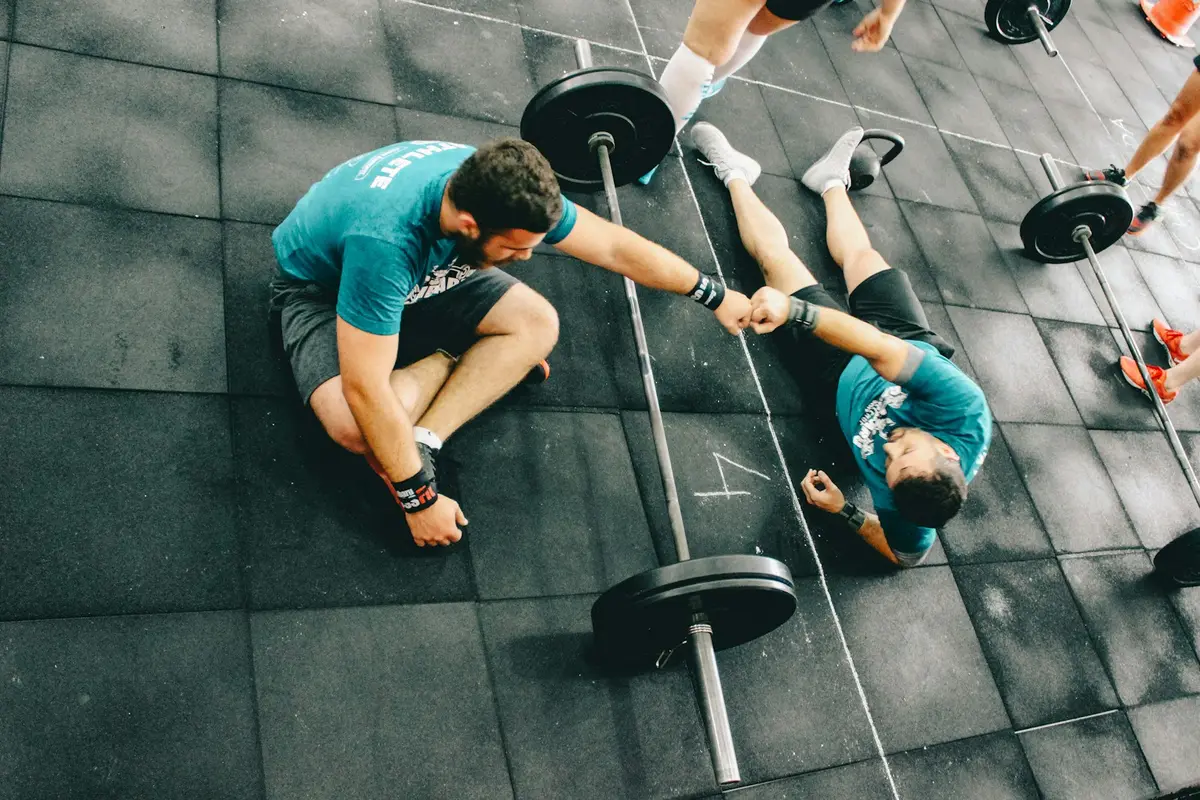 Two members on the floor after a workout, fist-bumping next to a loaded barbell