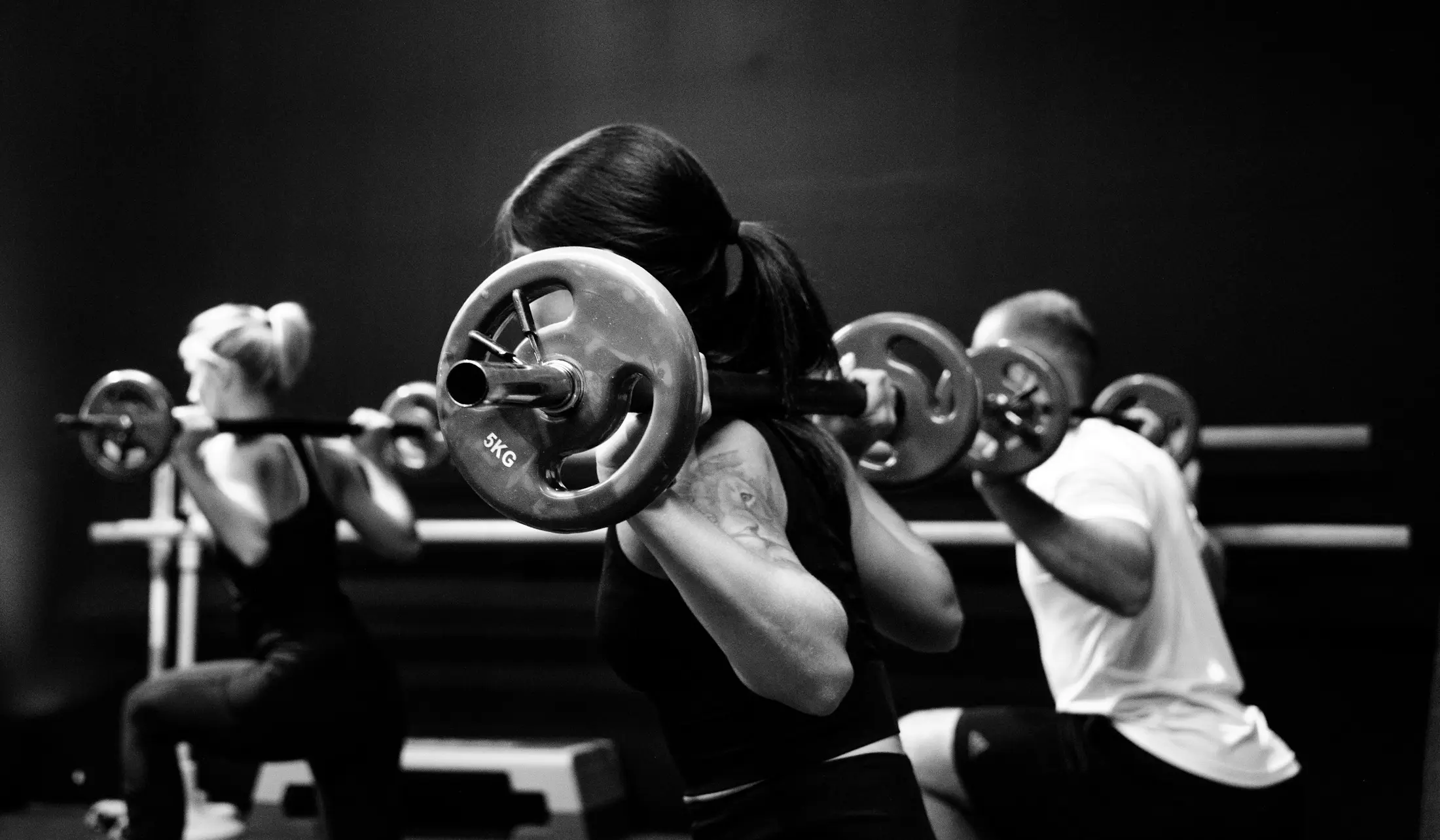 Three members holding barbells on their backs during a strength class