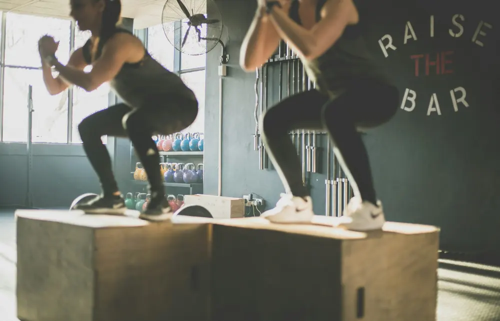 Two members doing box jumps side by side on wooden boxes