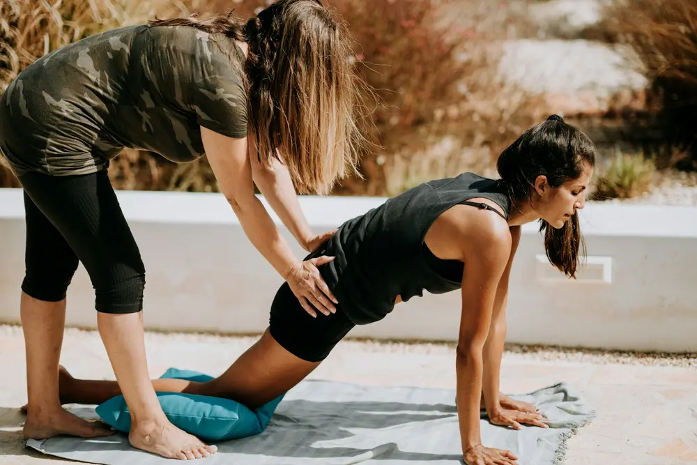 Coach guiding a member through a hip stretch on a mat