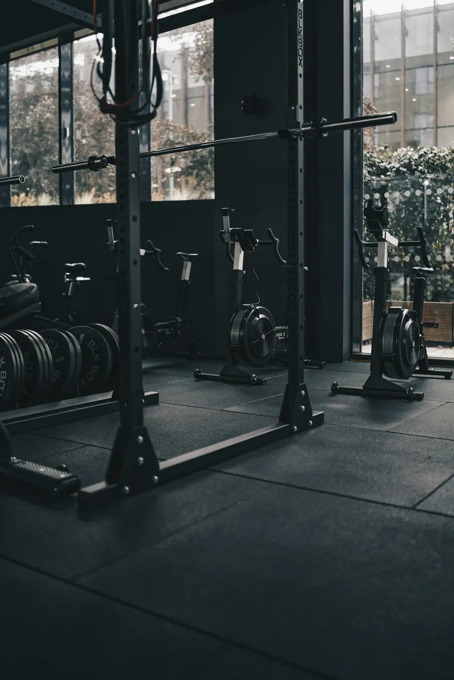 Row of squat racks with plates loaded, lit by tall windows