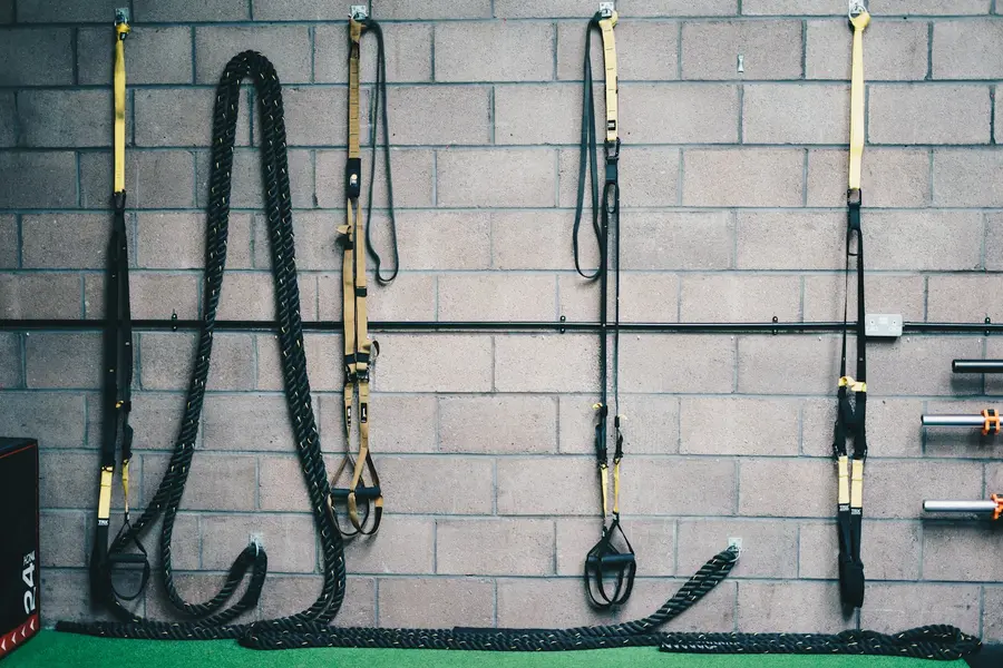 Battle ropes and suspension trainers hanging on a block wall above turf