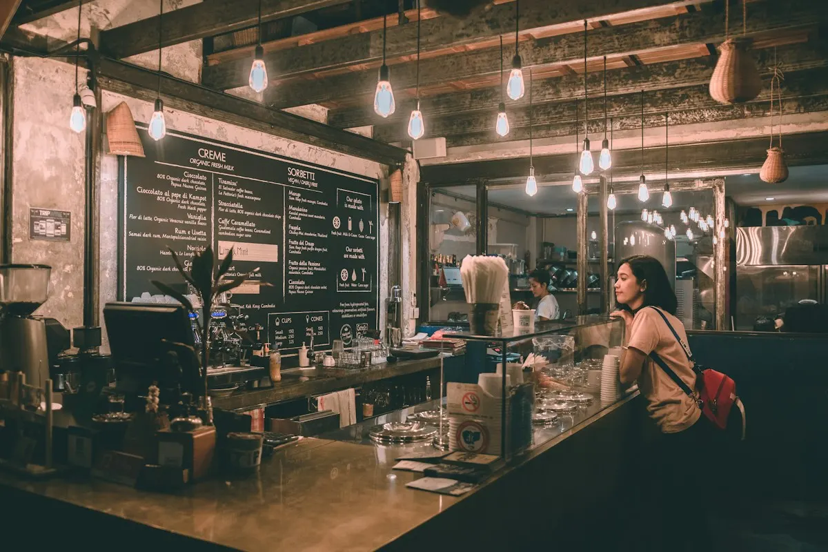 Warm café counter under bare bulbs, with a customer ordering at the bar