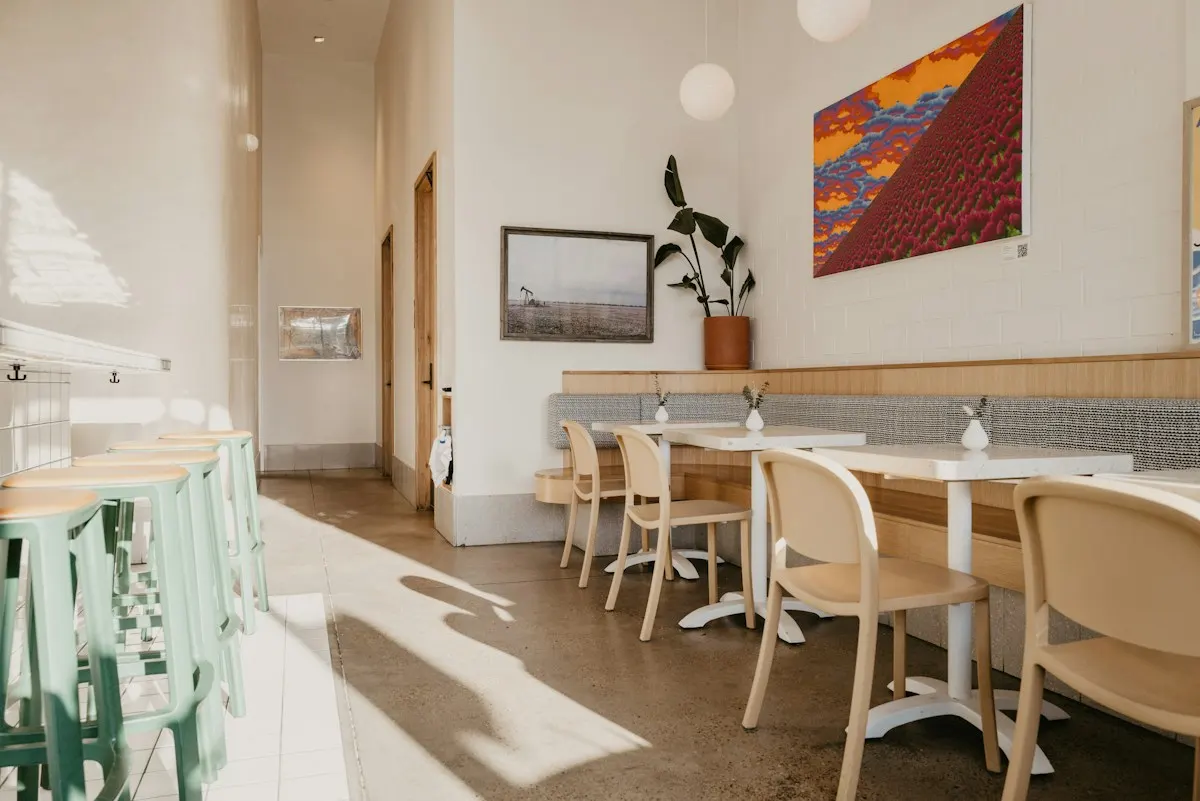Bright café interior with wooden tables, pale chairs and a colourful painting