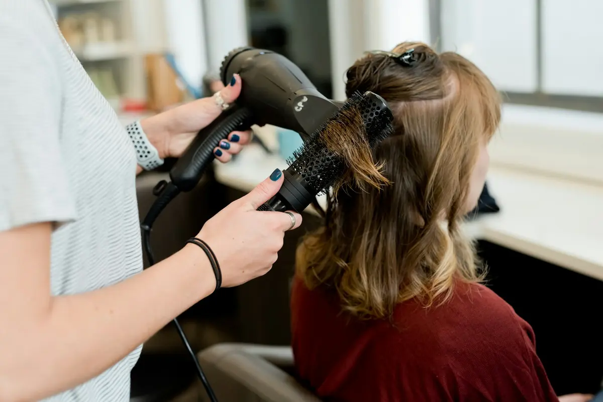 Close-up of a round brush and hairdryer smoothing a client’s hair