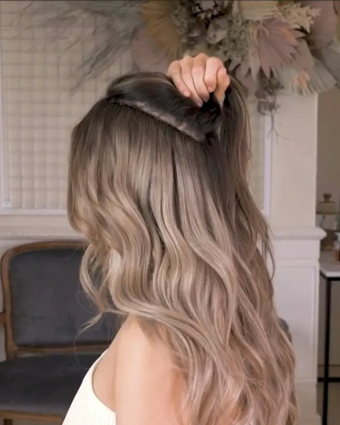 Long, soft ash-blonde waves pinned back at the crown, seen from behind in the salon