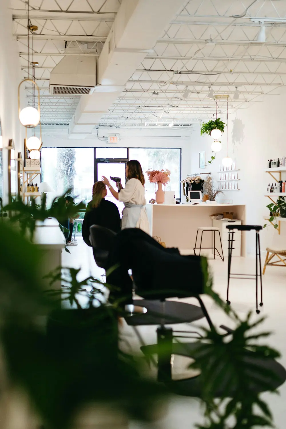 The bright salon floor with plants, styling chairs and a stylist working near the front window