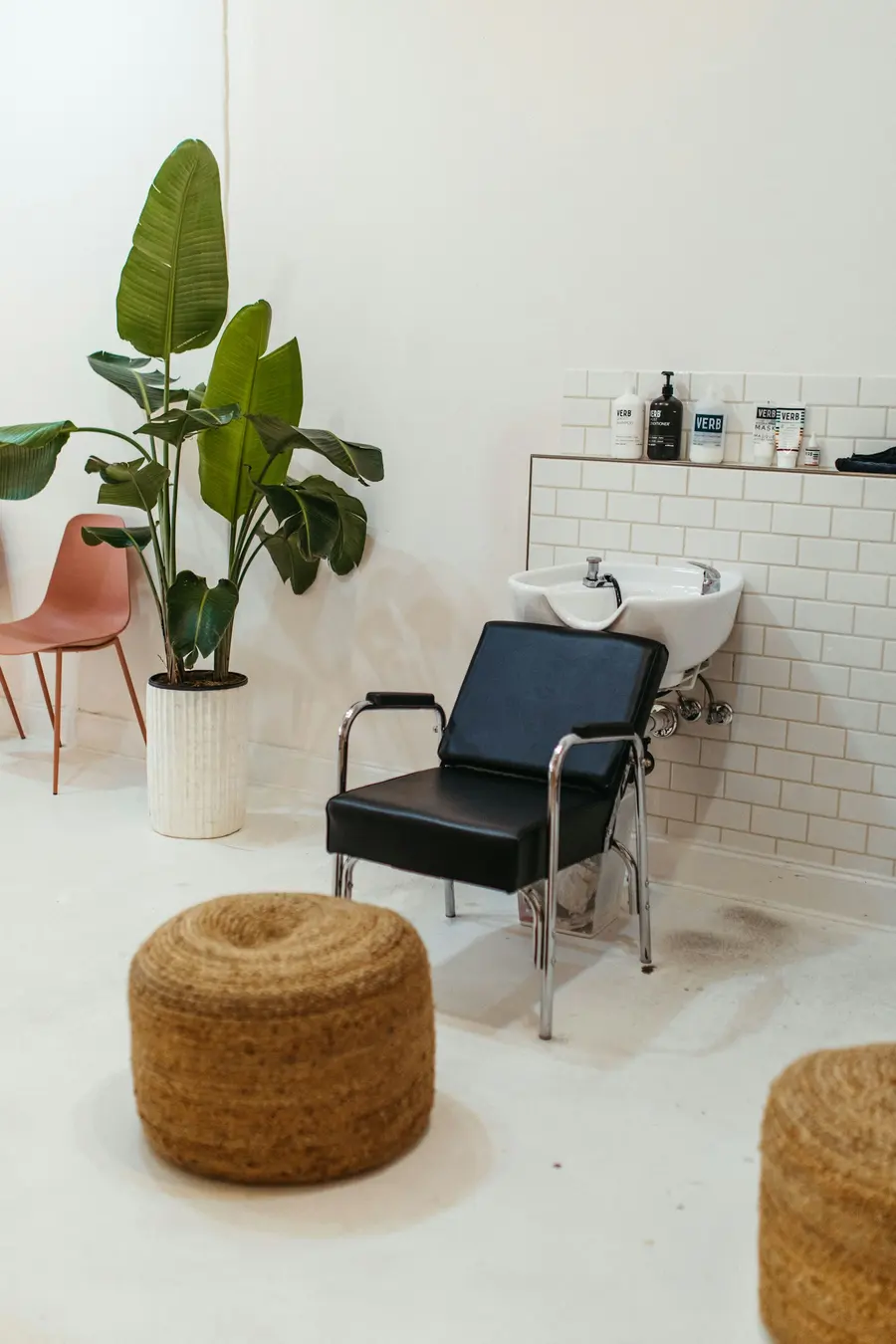 Quiet wash station with a black chair, white tiles, woven poufs and a large plant