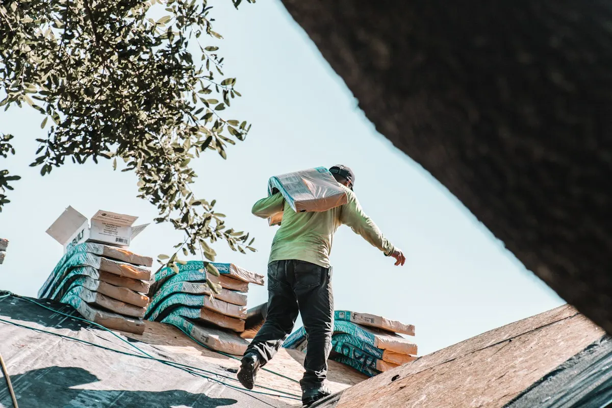 A roofer carrying a bundle of shingles up a steep roof