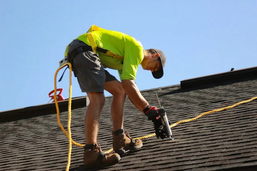A roofer nailing down shingles while clipped to a safety line