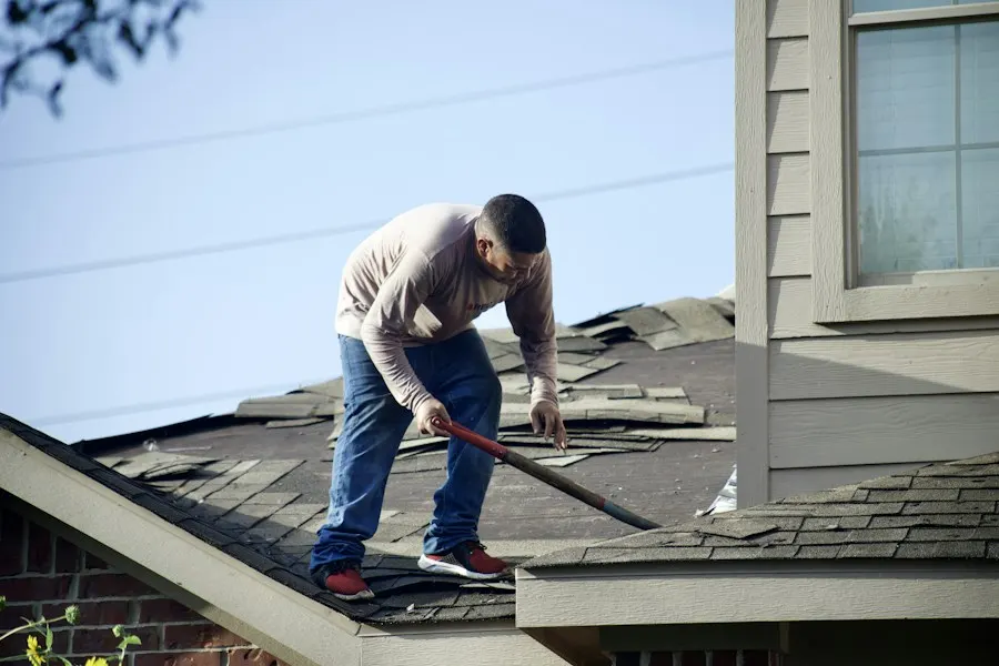A roofer tearing off old shingles with a shovel